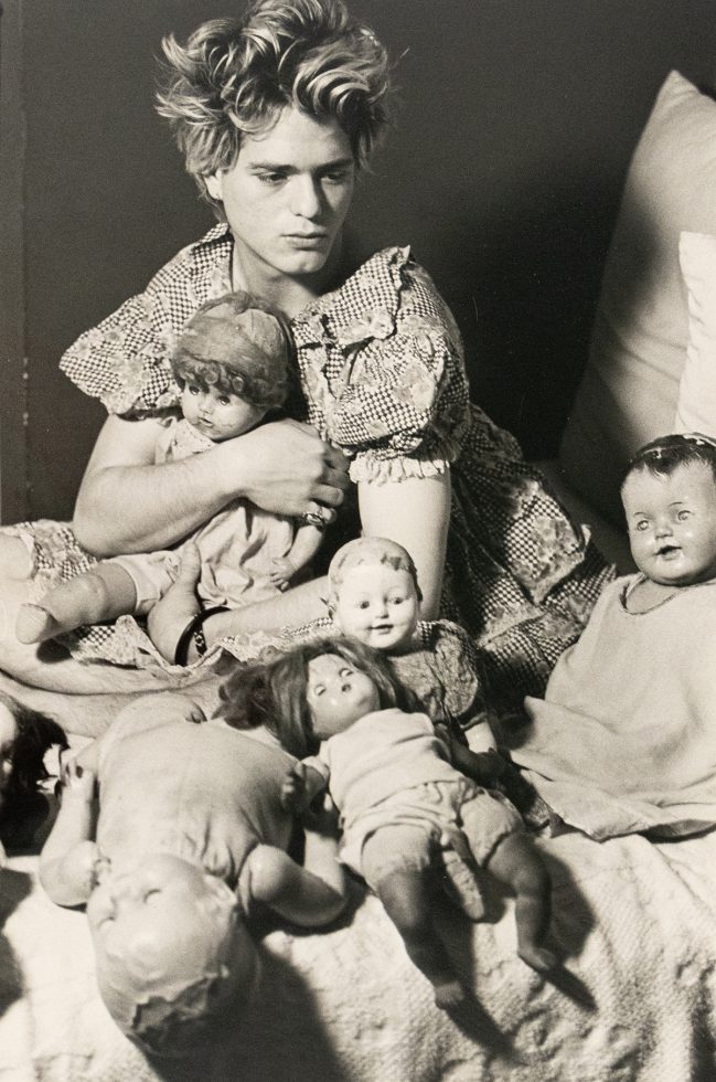 A black and white photograph of a boy in a gingham shirt with various toy dolls.