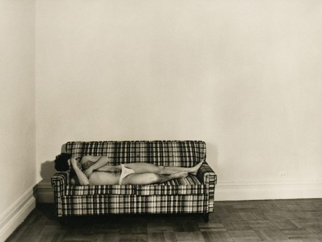 A black and white photograph of a man in white underwear lying on a sofa.