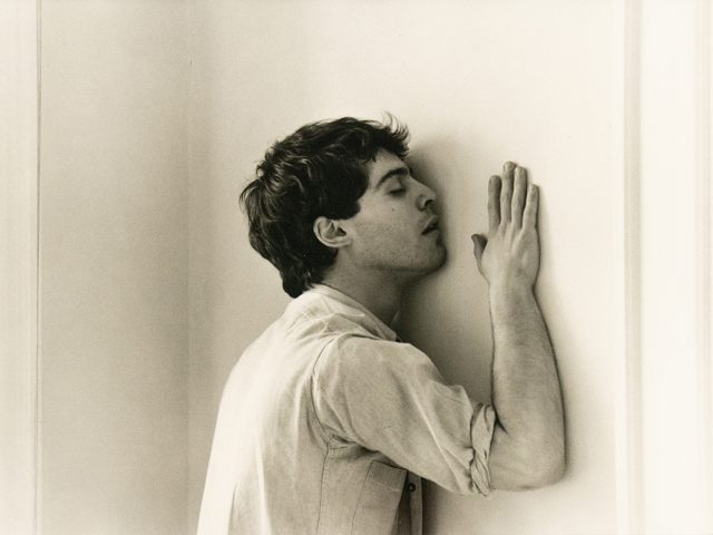 A black and white photograph of a man caressing a wall.