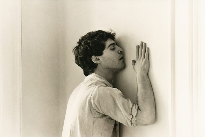 A black and white photograph of a man caressing a wall.