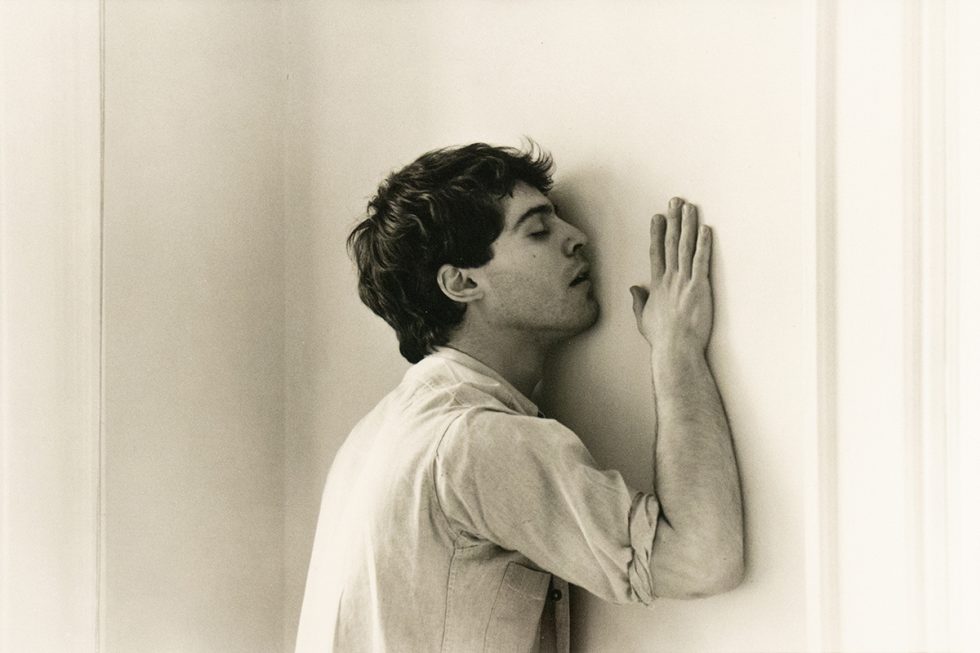 A black and white photograph of a man caressing a wall.