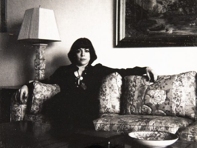 A back and white photograph of a woman with short black hair sitting on a sofa.
