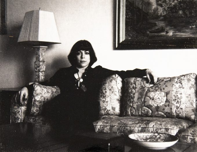 A back and white photograph of a woman with short black hair sitting on a sofa.