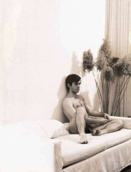 A black and white photograph of a young man sitting in a bed.