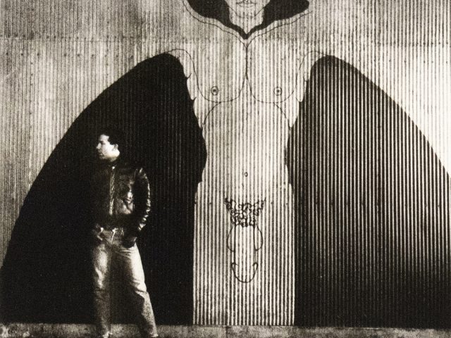 A black and white photograph of nude man in an industrial setting.