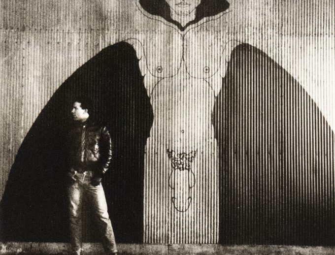 A black and white photograph of nude man in an industrial setting.