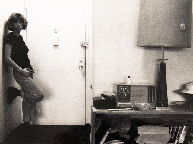 A black and white photograph of a woman standing by a front door.