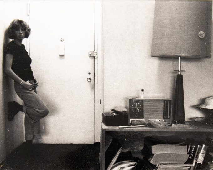 A black and white photograph of a woman standing by a front door.