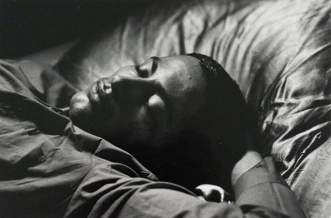 A black and white close-up photograph of a man sleeping in bed. His eye are closed and his expression is soft.