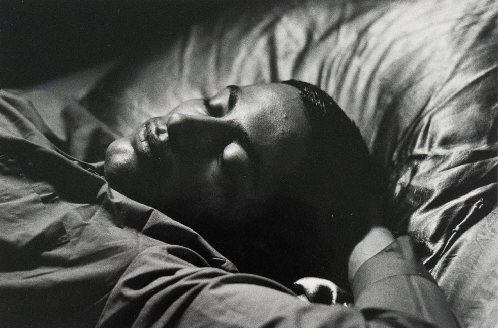 A black and white close-up photograph of a man sleeping in bed. His eye are closed and his expression is soft.