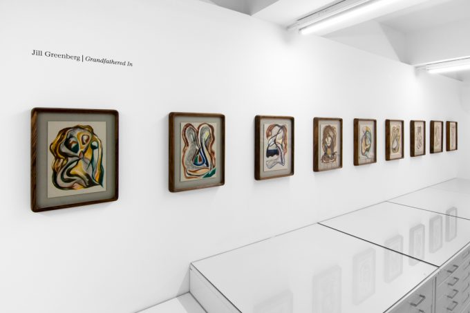 A series of abstract framed drawings hang on a white gallery wall under a black and white artist name and exhibition title.