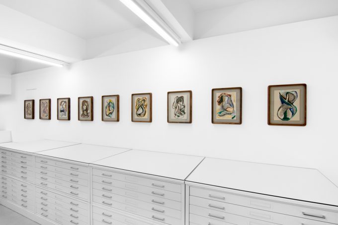 A series of abstract framed drawings hang on a white gallery wall under a black and white artist name and exhibition title.