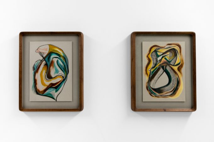 A series of abstract framed drawings hang on a white gallery wall under a black and white artist name and exhibition title.