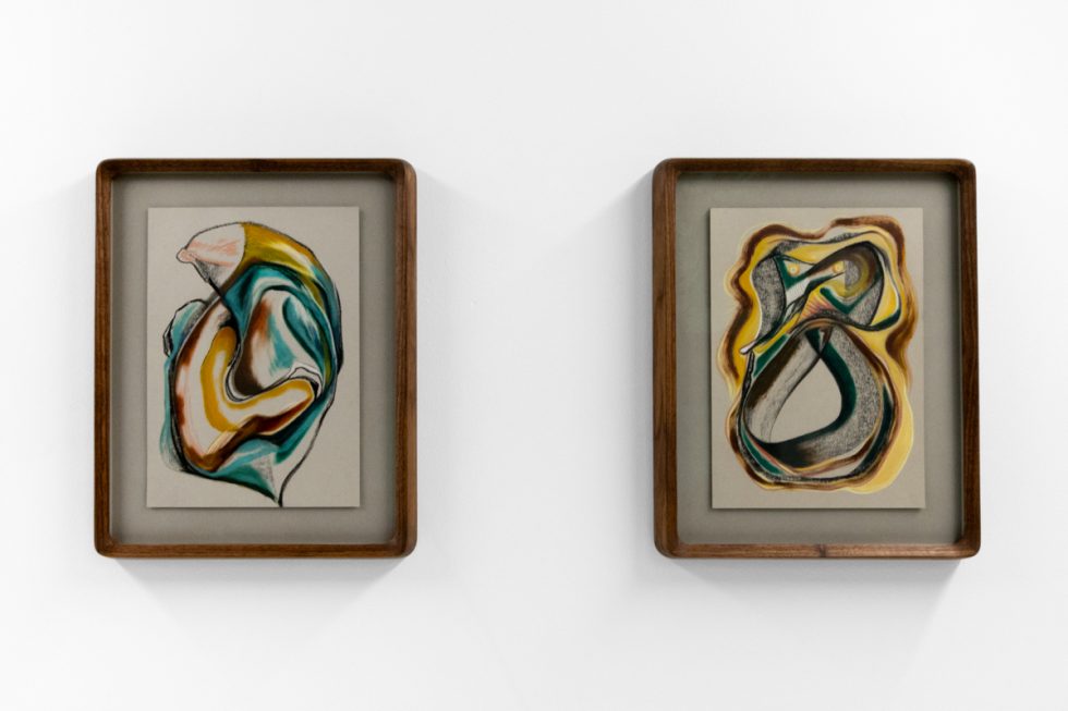 A series of abstract framed drawings hang on a white gallery wall under a black and white artist name and exhibition title.