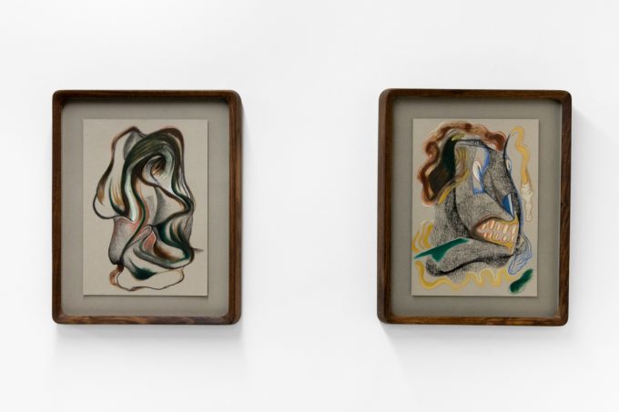 A series of abstract framed drawings hang on a white gallery wall under a black and white artist name and exhibition title.