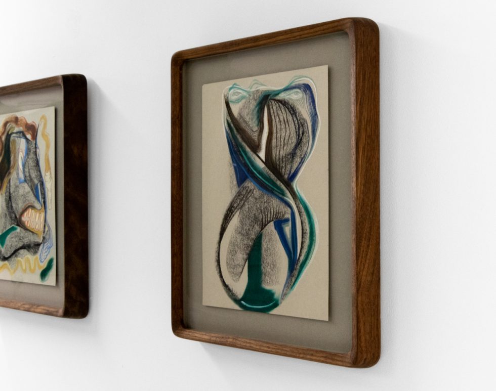 A series of abstract framed drawings hang on a white gallery wall under a black and white artist name and exhibition title.