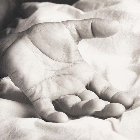 An open hand rests palm-up on a soft, rumpled fabric surface in gentle light.
