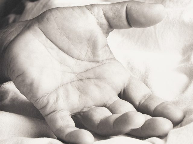 An open hand rests palm-up on a soft, rumpled fabric surface in gentle light.