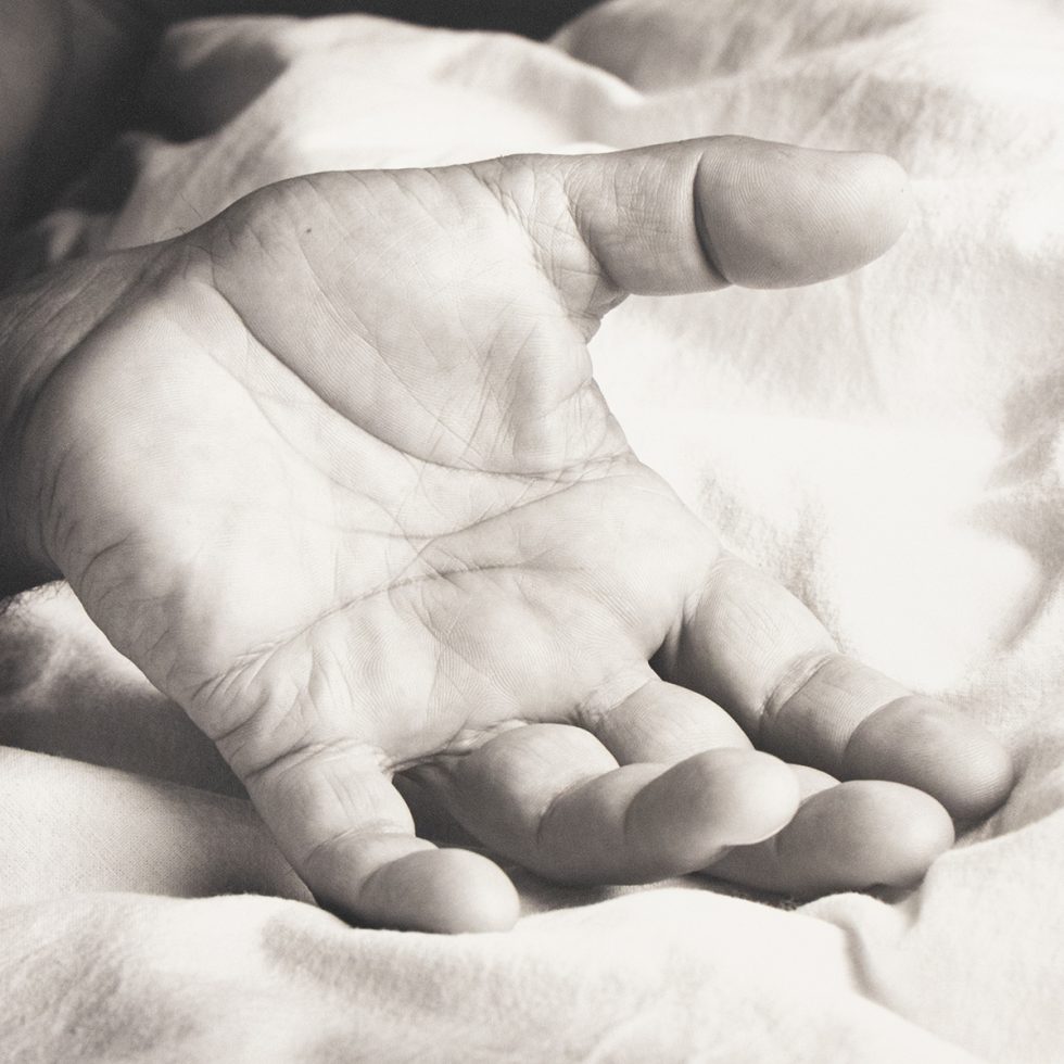 An open hand rests palm-up on a soft, rumpled fabric surface in gentle light.