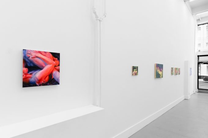 Colorful paintings hang on bright white gallery walls with grey floors.