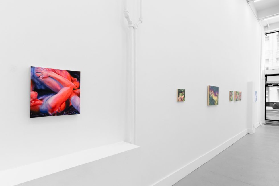 Colorful paintings hang on bright white gallery walls with grey floors.
