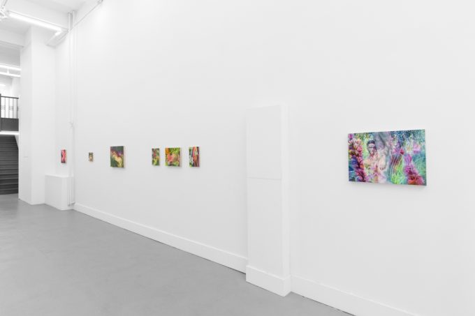 Colorful abstract paintings hang on a white gallery wall, ending with a larger piece featuring a surreal scene with a semi-nude figure.