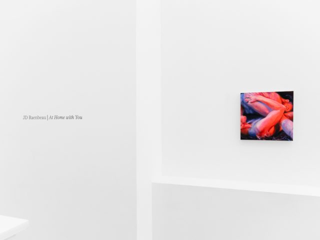 A colorful painting on a white gallery wall with wall text beside it.