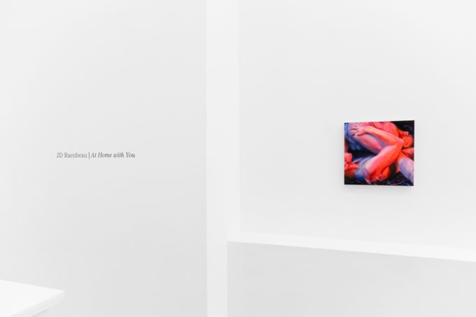 A colorful painting on a white gallery wall with wall text beside it.