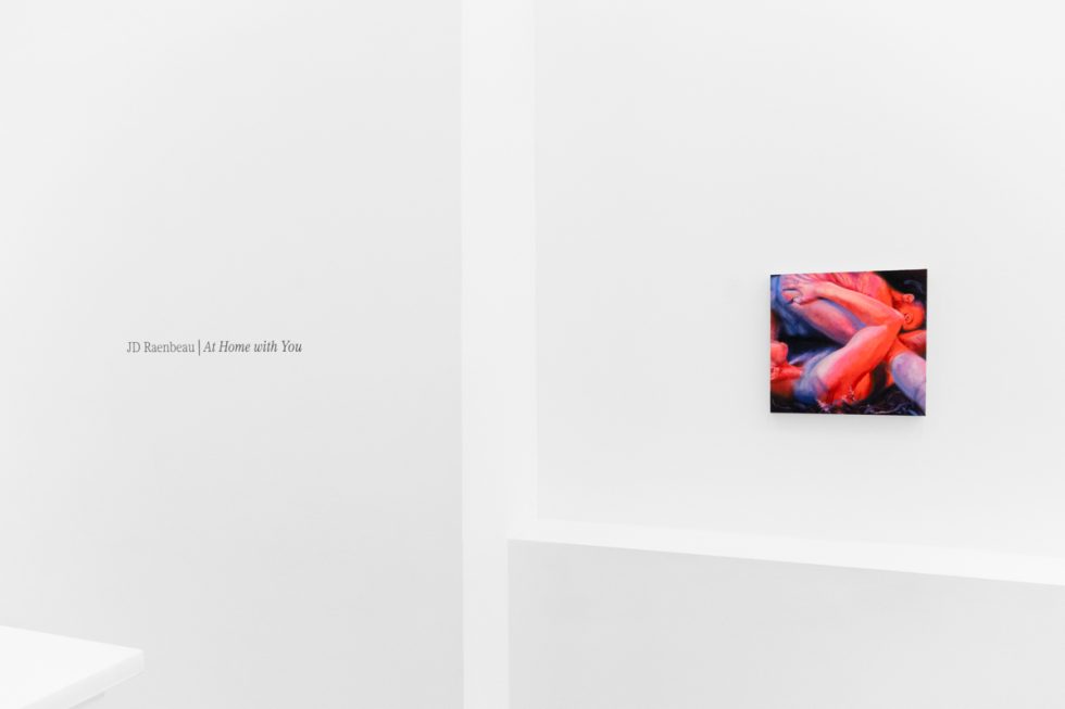 A colorful painting on a white gallery wall with wall text beside it.