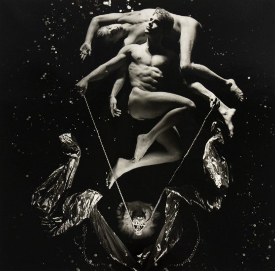 A black and white photograph of two nude men in a black abyss with splashes of light in the darkness.