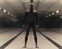 Underwater figure stands powerfully at the bottom of an empty pool, framed by lane lines and dramatic light, with fists clenched and legs apart.