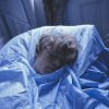 A fair-skinned person with curly blond hair sleeps soundly, covered in light blue sheets and illuminated by a cool, blue light.