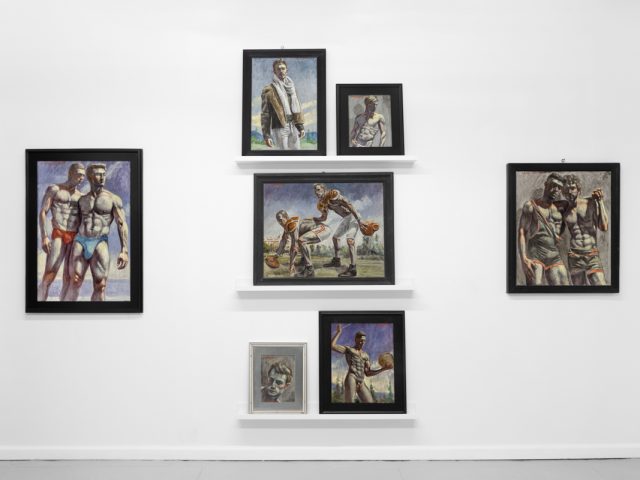Seven framed paintings of muscular men in athletic or intimate poses are arranged on a white wall with three display shelves.