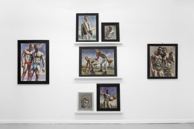 Seven framed paintings of muscular men in athletic or intimate poses are arranged on a white wall with three display shelves.