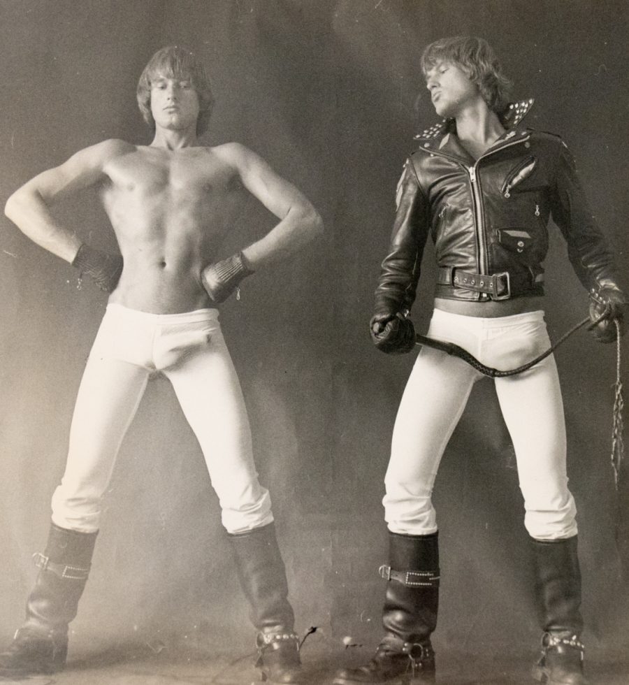 A black and white photograph of two men in white tights, one in a leather jacket.