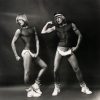 Two figures with similar features, one in a head covering, display athletic forms in striking poses against a plain background.