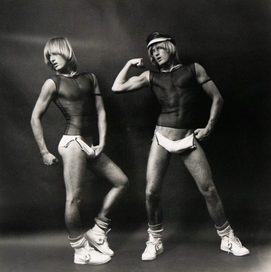 Two figures with similar features, one in a head covering, display athletic forms in striking poses against a plain background.