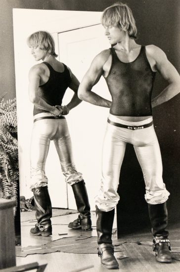 A black and white photograph of a man in a black tank top and silver metallic pants.