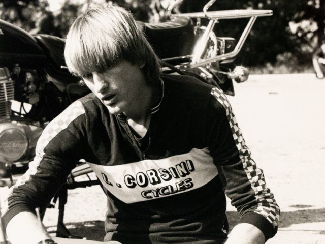 A black and white portrait of a man with a bowl cut sitting by a motorcycle.