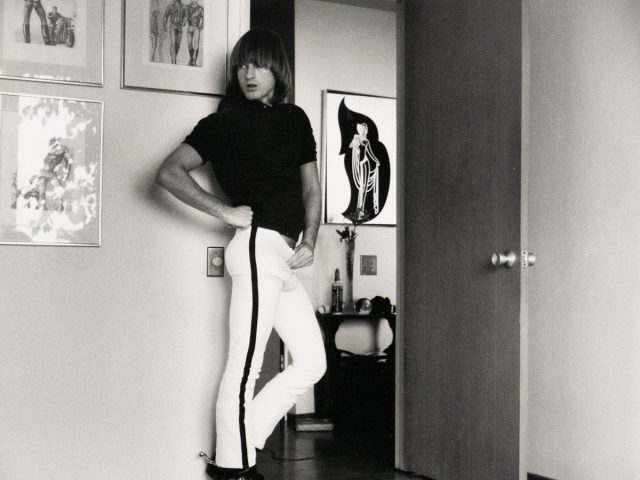 Person posing confidently in a room decorated with bold artwork and fashion illustrations.