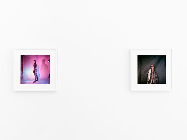 Brightly lit gallery with colorful, surreal portraits in white frames displayed along stark white walls.