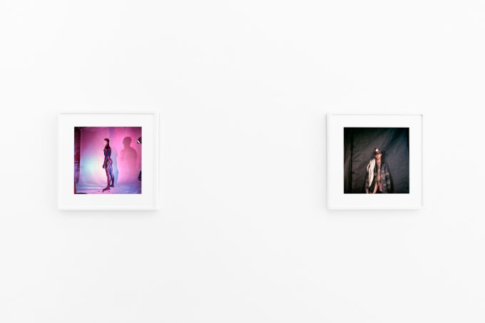 Brightly lit gallery with colorful, surreal portraits in white frames displayed along stark white walls.