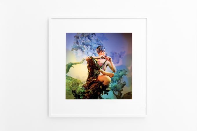 Brightly lit gallery with colorful, surreal portraits in white frames displayed along stark white walls.