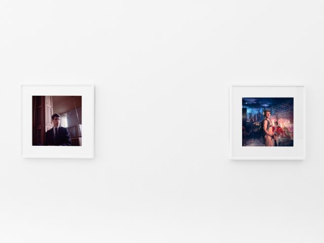 Brightly lit gallery with colorful, surreal portraits in white frames displayed along stark white walls.