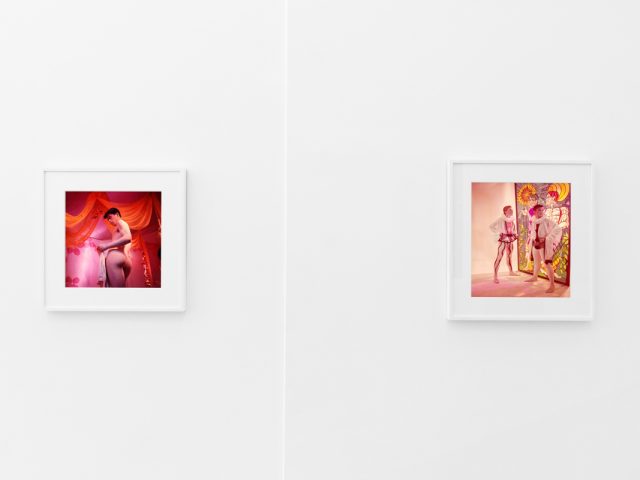 Brightly lit gallery with colorful, surreal portraits in white frames displayed along stark white walls.