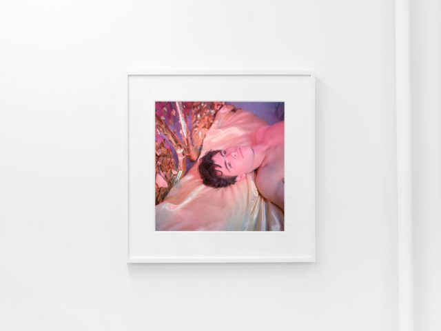 Brightly lit gallery with colorful, surreal portraits in white frames displayed along stark white walls.