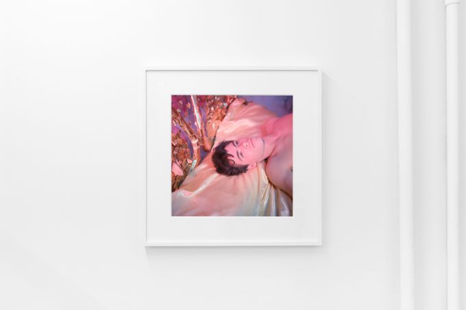 Brightly lit gallery with colorful, surreal portraits in white frames displayed along stark white walls.
