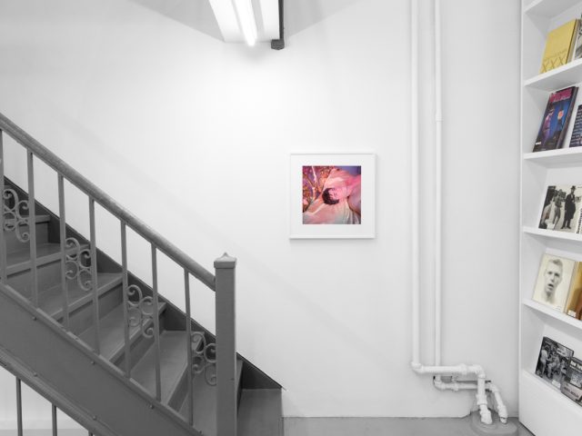 Brightly lit gallery with colorful, surreal portraits in white frames displayed along stark white walls.