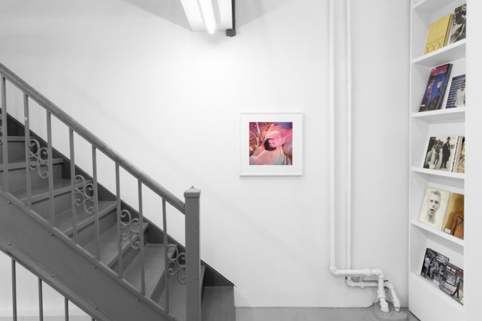 Brightly lit gallery with colorful, surreal portraits in white frames displayed along stark white walls.