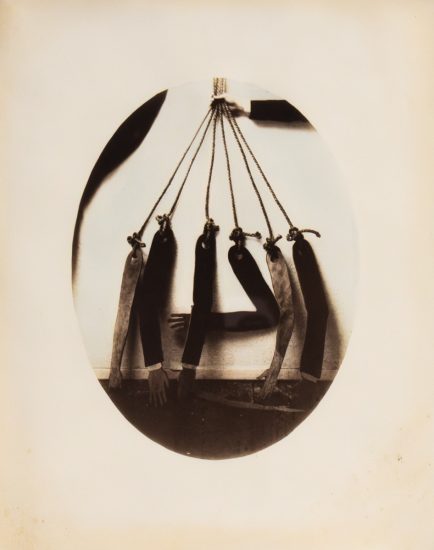 This is an old, somewhat blurry black and white photo of seven dismembered arms hanging by strings.